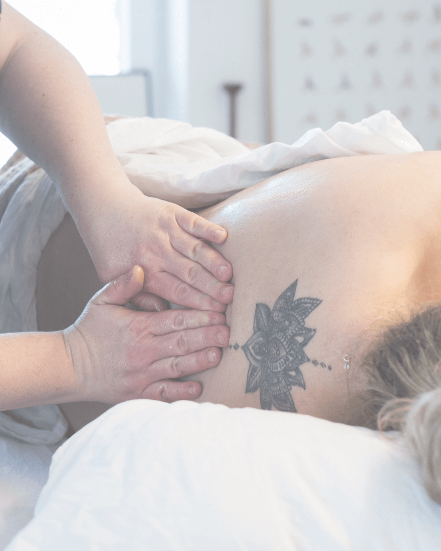 Jordemoder Ina giver gravid kvinde rygmassage. Kvinden ligger på siden på briksen.